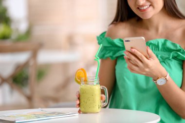 Genç kadın cep telefonuyla içme lezzetli sağlıklı güler yüzlü süre masada kapalı