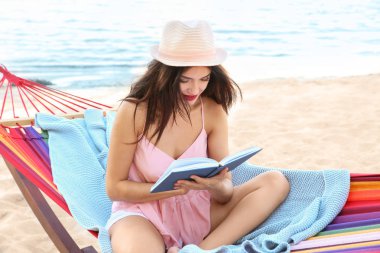 Genç kadın, sahil hamakta kitap okumak