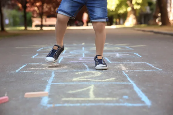 Little child playing hopscotch drawn with colorful chalk on asphalt