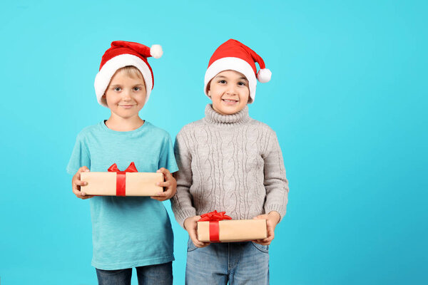 Cute little children in Santa hats with Christmas gifts on color background
