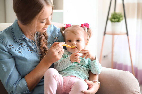 Caring mother feeding her cute little baby with healthy food at home