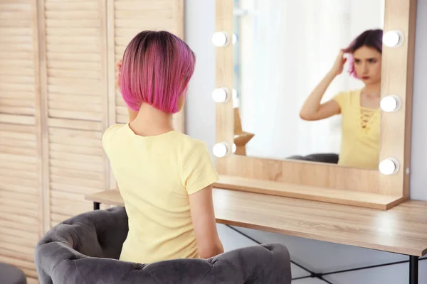 Young woman with color hair looking into mirror in beauty salon. Modern trend