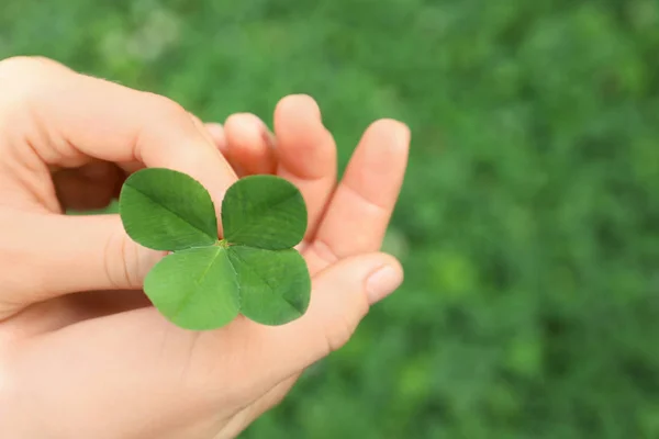 Woman holding four-leaf clover outdoors, closeup with space for text