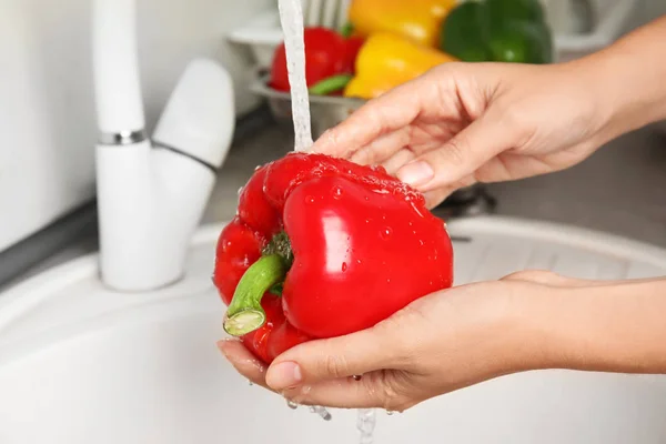 Woman washing paprika pepper in kitchen sink, closeup