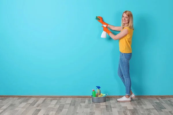 Woman in gloves cleaning color wall with sponge