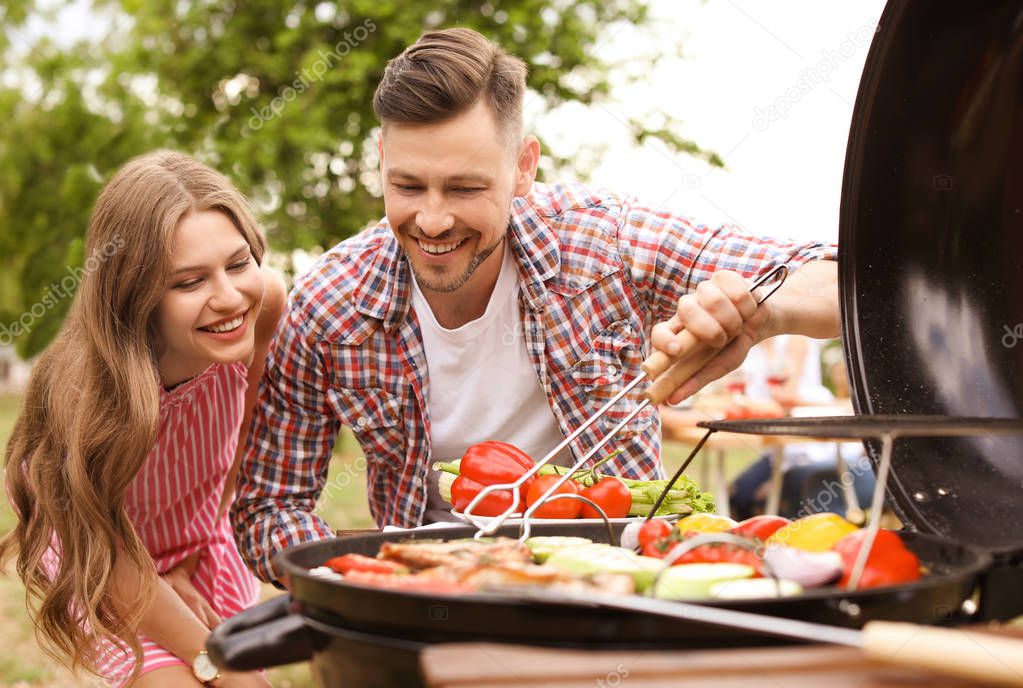 Young couple having barbecue with modern grill outdoors