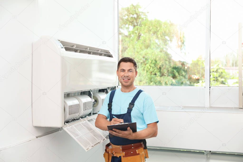 Technician with clipboard near air conditioner indoors