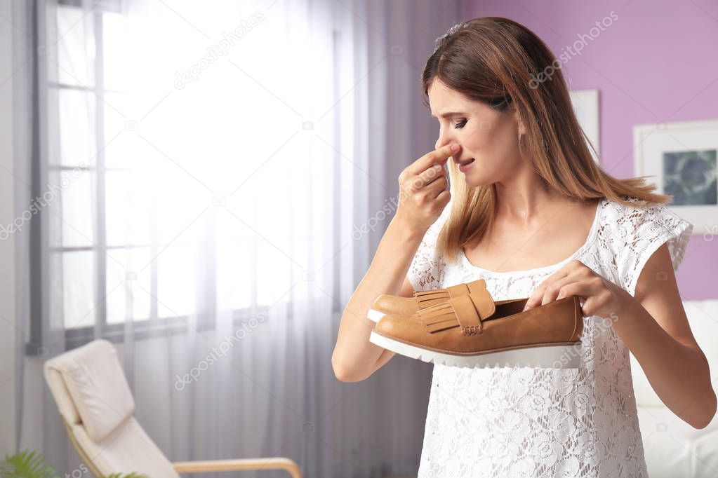 Woman feeling bad smell from shoes at home. Air freshener