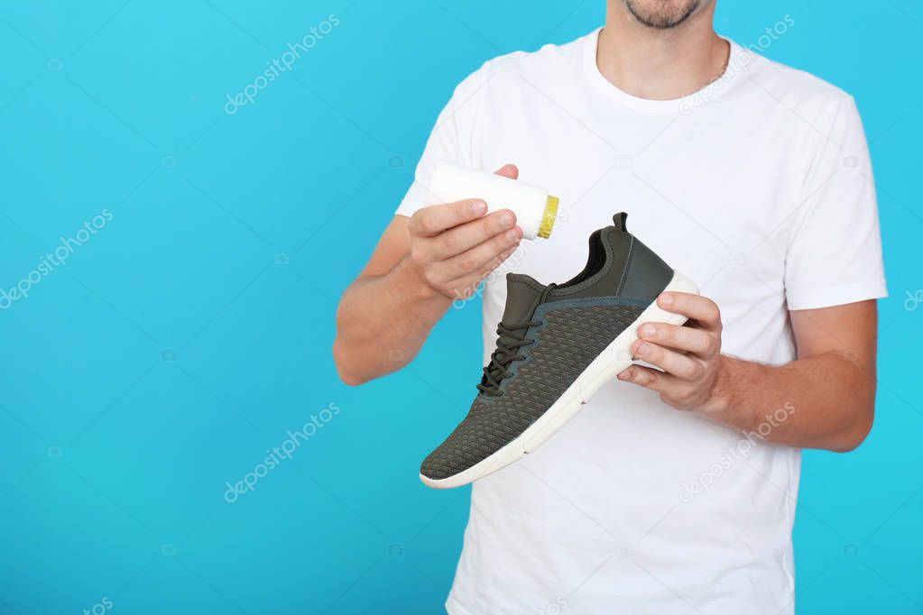 Man putting powder freshener into shoe on color background