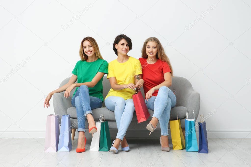 Group of young women with shopping bags sitting on sofa near light wall