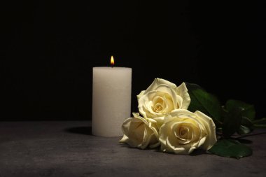 Beautiful white roses and candle on table against black background. Funeral symbol clipart
