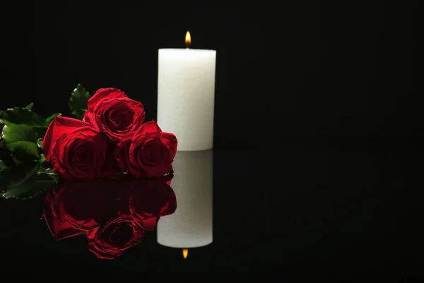Beautiful red roses and candle on black background. Funeral symbol
