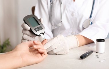 Doktor masadaki glukometreyle kan şekerini ölçüyor. Diyabet testi