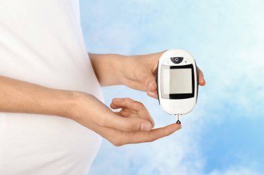Pregnant woman checking blood sugar level with glucometer on color background. Diabetes test clipart
