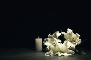 Beautiful lilies and burning candle on dark background with space for text. Funeral flowers clipart