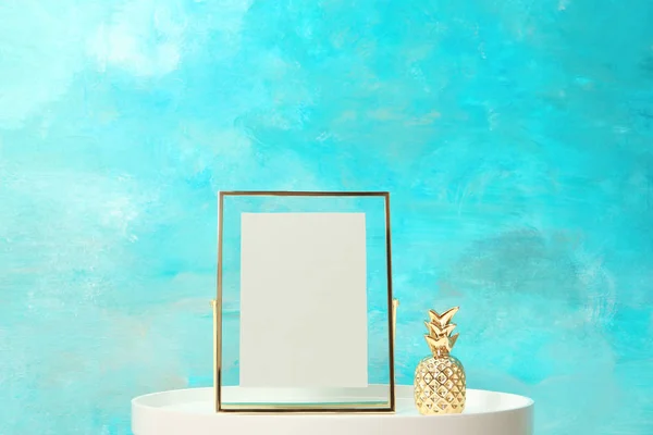 Blank frame and decorative pineapple figure on table near color wall. Mock up for design