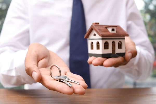 Real estate agent holding house model and keys at table
