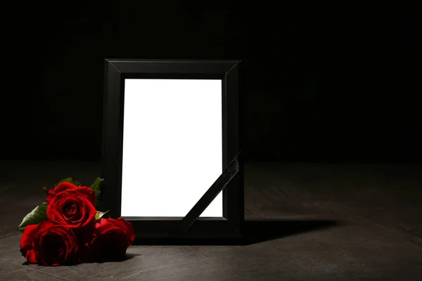 Empty frame with black ribbon and roses on table. Funeral symbol
