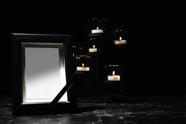 Funeral photo frame and burning candles in holder on dark background