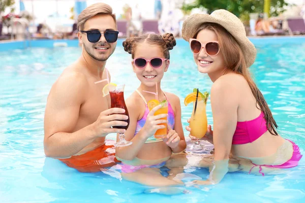 Happy family with cocktails in pool on sunny day