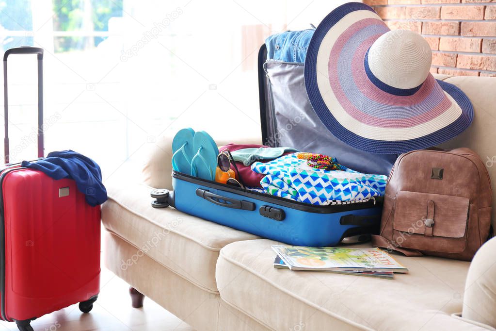 Open suitcase with different clothes and accessories on sofa indoors. Packing for vacation