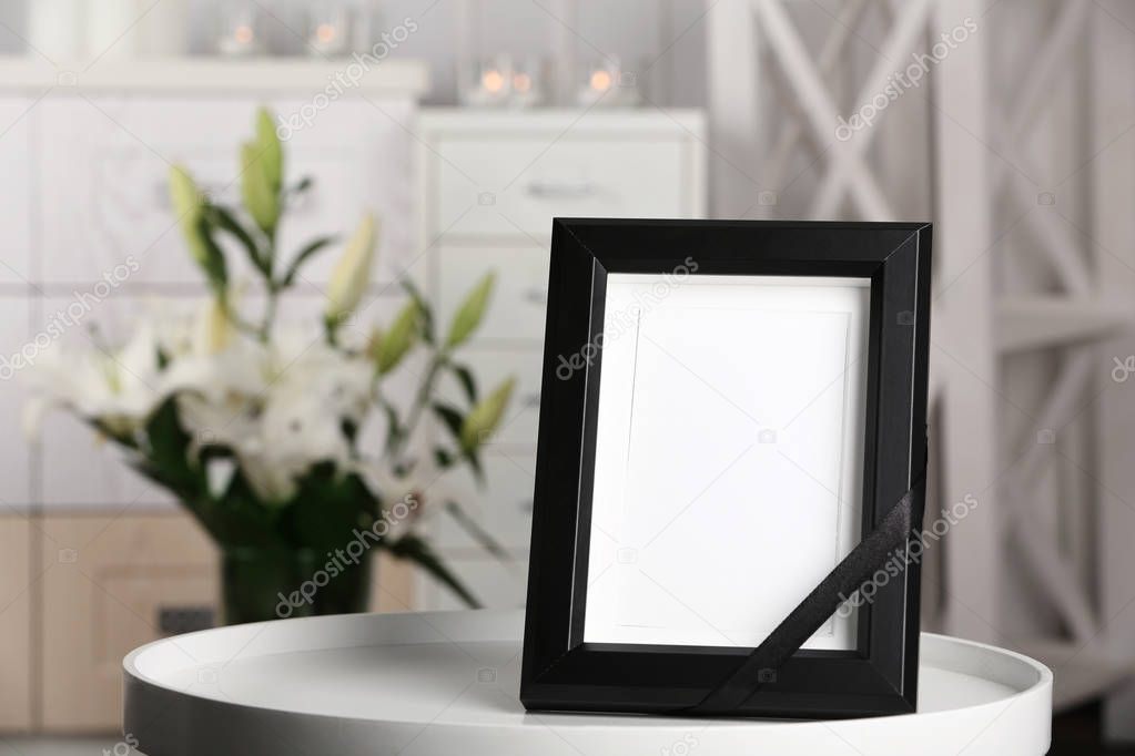 Funeral photo frame with black ribbon on table, indoors