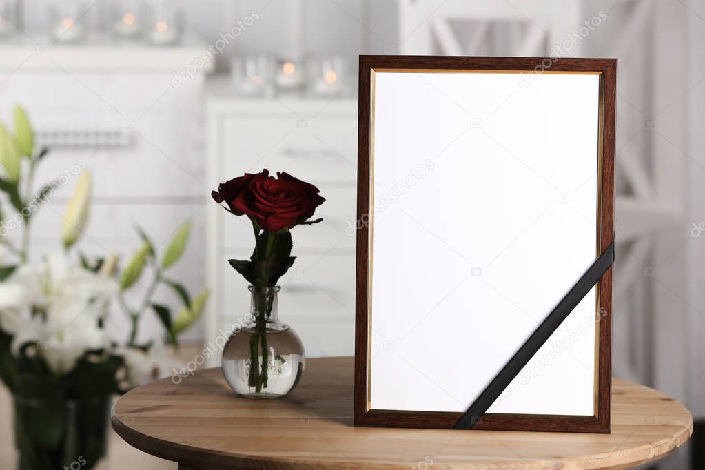 Funeral photo frame with black ribbon and roses on table, indoors