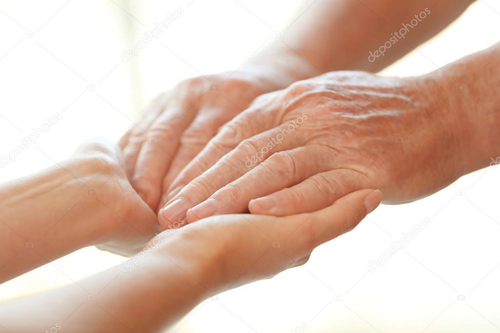 Young woman holding elderly man hands on blurred background, closeup. Help service