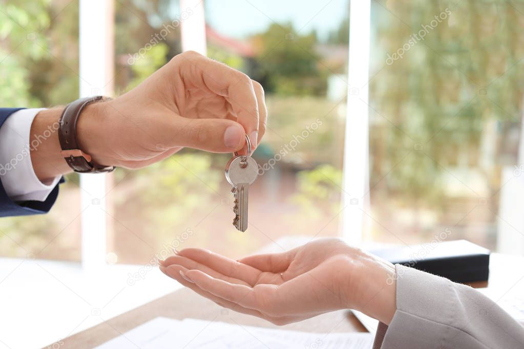 Real estate agent giving key to woman in office, closeup