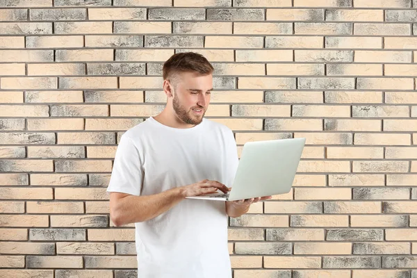 Young handsome man with laptop on brick wall background