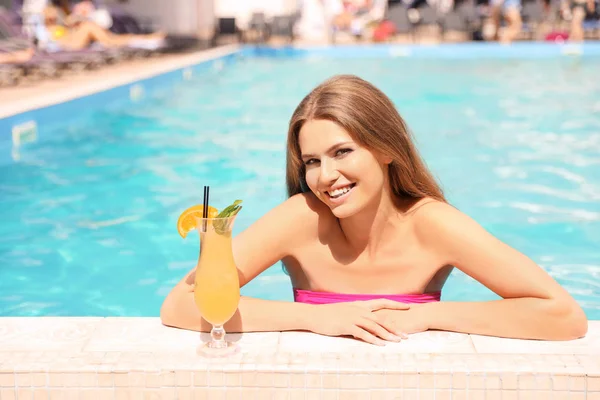 Young woman with cocktail in pool on sunny day