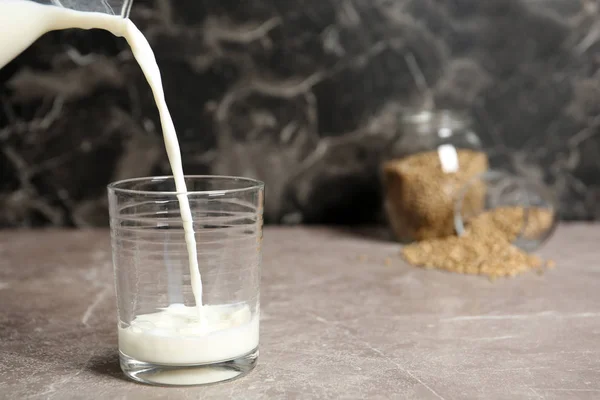 Pouring hemp milk into glass on table, closeup