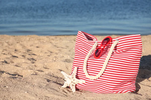 Bag with beach objects on sand near sea. Space for text