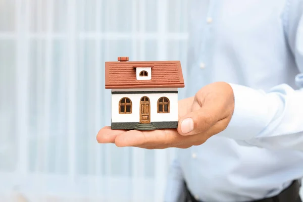 Immobilienmakler Hält Hausmodell Auf Verschwommenem Hintergrund — Stockfoto