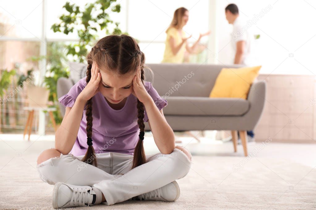 Upset child sitting on floor while parents fighting on background. Family relationships