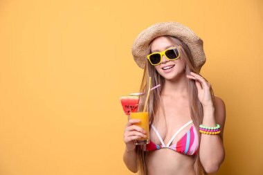 Güzel genç kadın bikini ve renk arka plan üzerinde kokteyl ile şapka