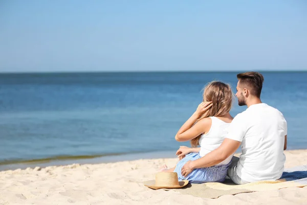 快乐的年轻夫妇坐在一起在海滩上阳光明媚的一天 — 图库照片
