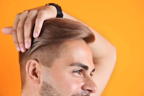 Young man with trendy hairstyle on color background, closeup