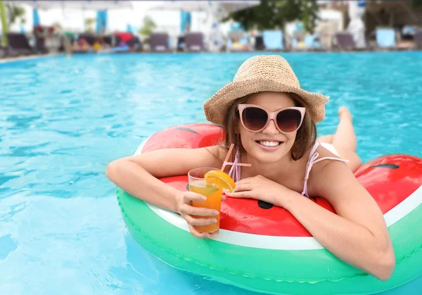 Young woman with cocktail in pool on sunny day