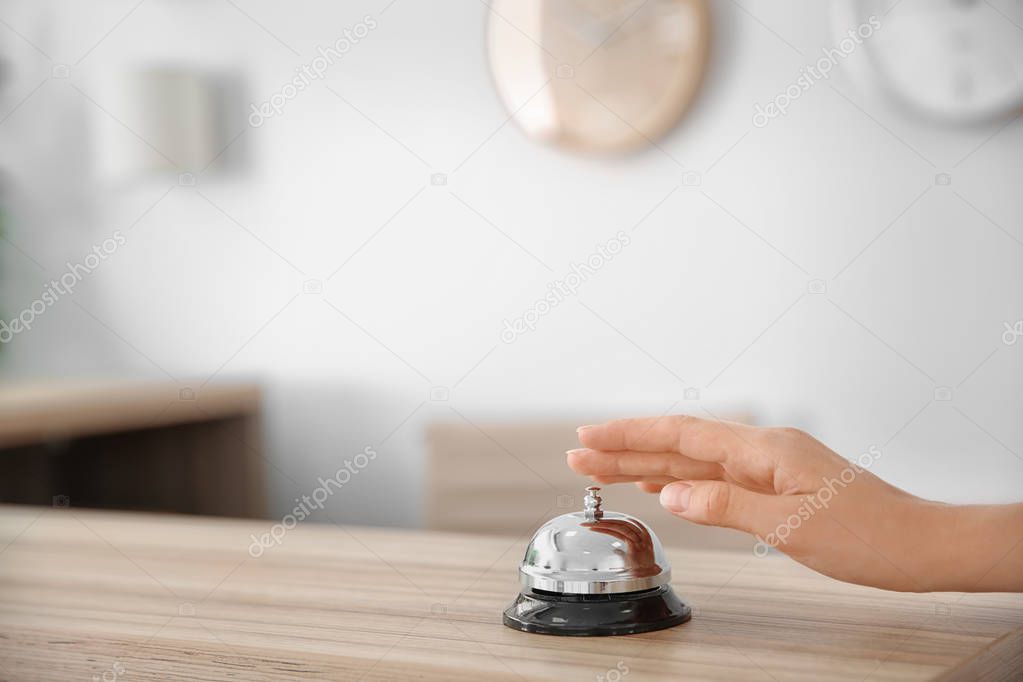 Woman ringing service bell on reception desk in hotel, closeup