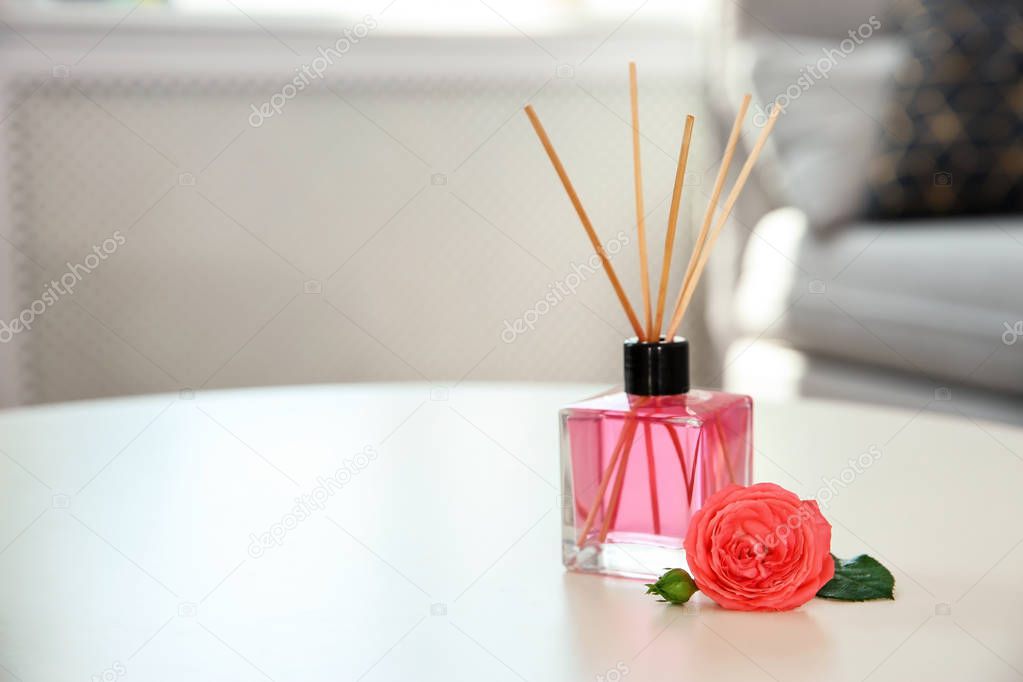 Aromatic reed air freshener and rose on table indoors