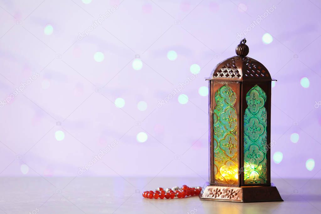 Muslim lamp Fanus with prayer beads and space for design on blurred lights background