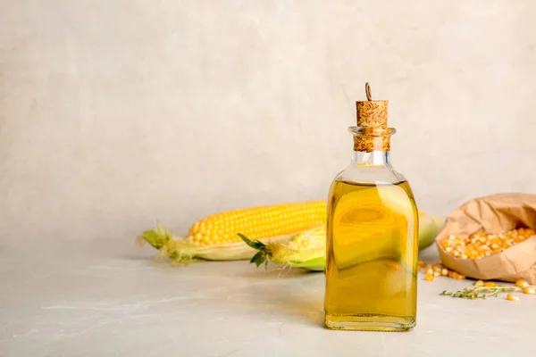 Bottle of corn oil and fresh cobs on table against light wall