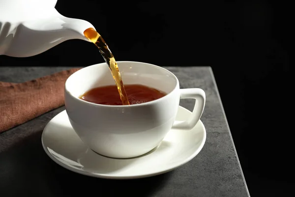 ダークウッドのテーブルの上に白い磁器カップに熱いお茶を注いでください — ストック写真