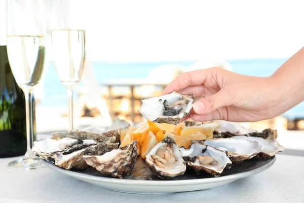 Woman holding fresh oyster over plate, focus on hand