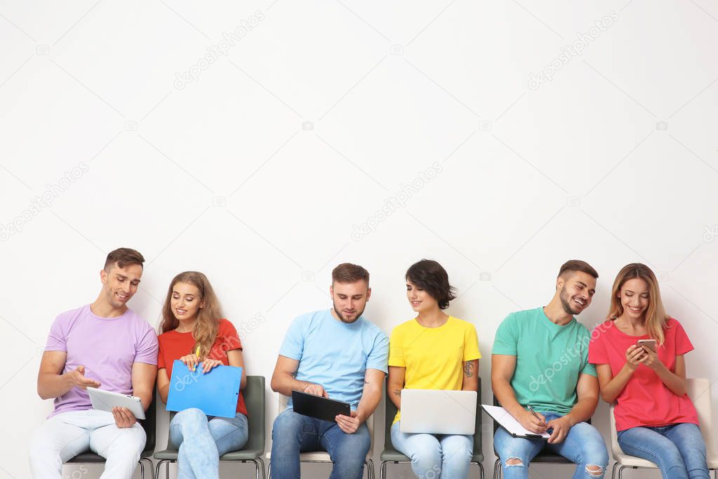 Group of young people waiting for job interview near light wall