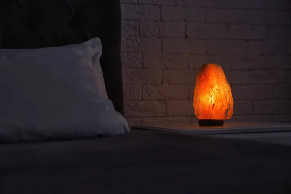 Himalayan salt lamp glowing on bedside table in dark room