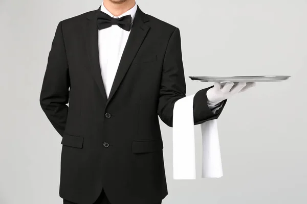 Waiter holding metal tray on light background