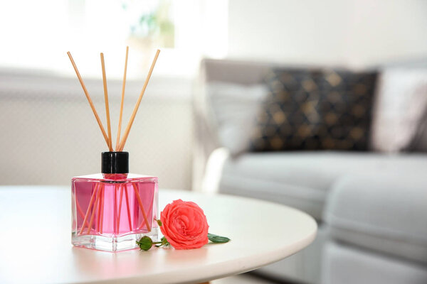 Aromatic reed air freshener and rose on table indoors