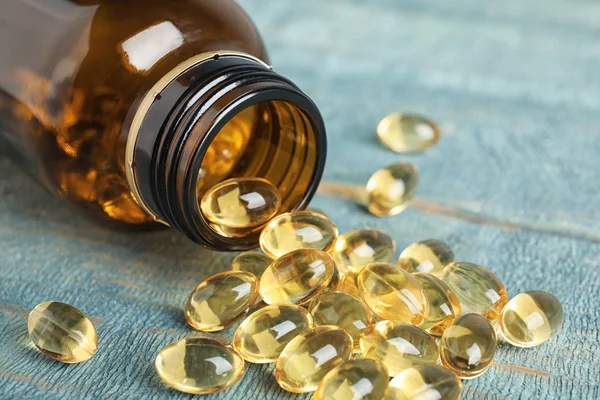 Bottle with cod liver oil pills on table, closeup